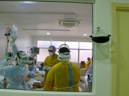 316 pessoas morreram na fila por leitos de UTI em Santa Catarina profissionais de saúde utilizando EPI em volta de paciente em cama vistos por grande janela de vidro em corredor
