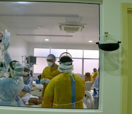 316 pessoas morreram na fila por leitos de UTI em Santa Catarina profissionais de saúde utilizando EPI em volta de paciente em cama vistos por grande janela de vidro em corredor