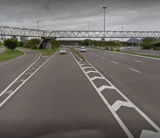 Na avenida, o asfalto cinza com marcações em branco, ao fundo a passarela do CIC, que deve passar por recuperação, de acordo com recomendação do MPSC