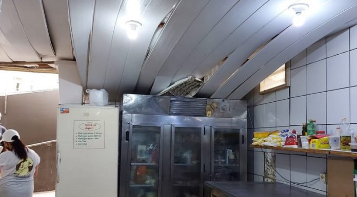 Foto mostra a cozinha de um estabelecimento com o forro caindo. Do lado direito duas bancadas e ao fundo geladeiras. A vigilância sanitária de florianópolis interditou uma padaria e um restaurante por higiene precária.