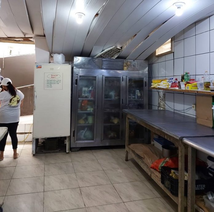 Foto mostra a cozinha de um estabelecimento com o forro caindo. Do lado direito duas bancadas e ao fundo geladeiras. A vigilância sanitária de florianópolis interditou uma padaria e um restaurante por higiene precária.