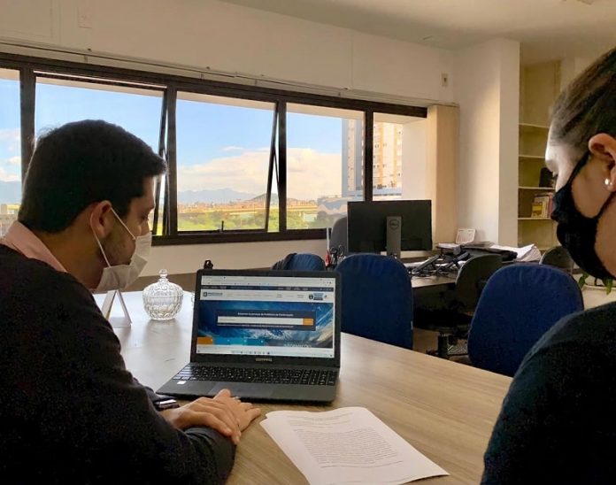 homem e mulher usando máscaras sentados em frente a notebook - programa de ensino prático do serviço público em florianópolis