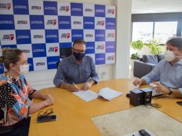 prefeito orvino na ponta de uma mesa assina documento, ao lado de secretário e da presidente da câmara de vereadores