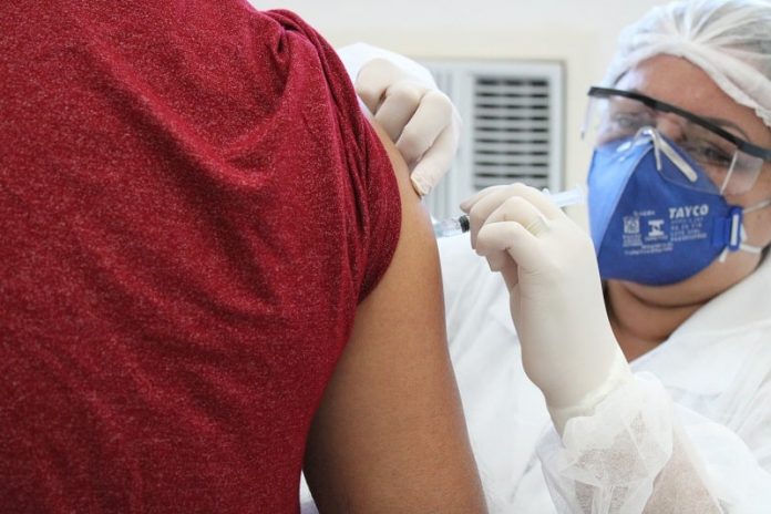 profissional de saúde usando máscara e óculos de proteção faz aplicação de vacina no braço de homem - são josé vacina contra influenza
