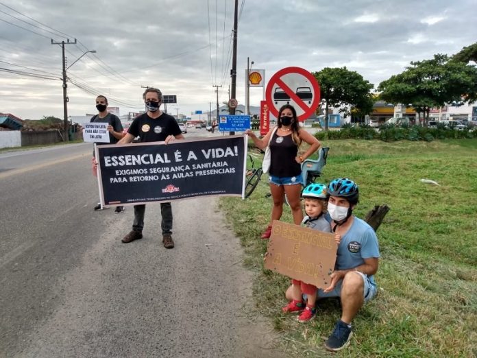 No acostamento de uma rua, grevistas seguram cartazes em que é possível ler 