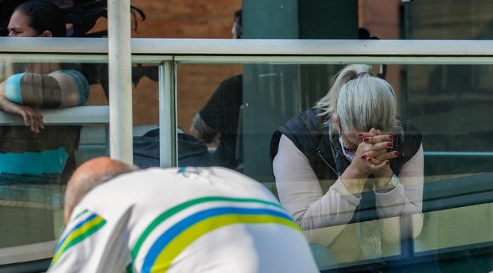 pessoas de cabeça baixa se lamentando em frente a hospital