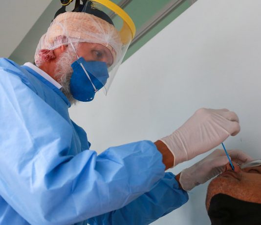 profissionais de saúde usando epi coloca cotonete no nariz de homem para testar para coronvírus