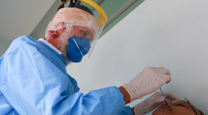 profissionais de saúde usando epi coloca cotonete no nariz de homem para testar para coronvírus