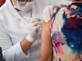 idosa recebe dose de vacina do braço aplicada por profissional de saúde usando epi - cidades vacinam público com 63 anos contra covid