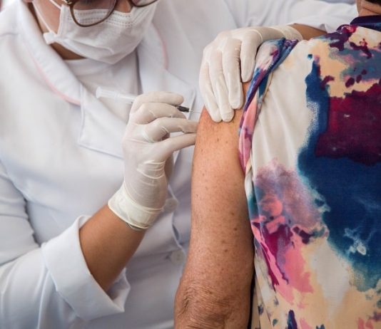 idosa recebe dose de vacina do braço aplicada por profissional de saúde usando epi - cidades vacinam público com 63 anos contra covid
