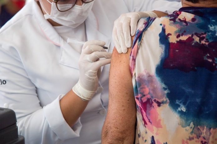 idosa recebe dose de vacina do braço aplicada por profissional de saúde usando epi - cidades vacinam público com 63 anos contra covid
