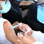 profissional de saúde aplica dose da vacina no braço de pessoa dentro do carro - vacinação de 64 anos contra coronavírus em Florianópolis