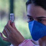 mulher usando máscara olha para ampola ao retirar dose de vacina - três meses de vacinação em sc