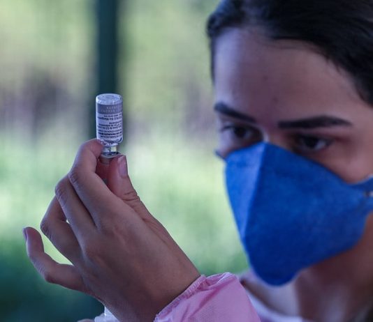 mulher usando máscara olha para ampola ao retirar dose de vacina - três meses de vacinação em sc