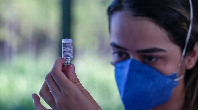 mulher usando máscara olha para ampola ao retirar dose de vacina - três meses de vacinação em sc