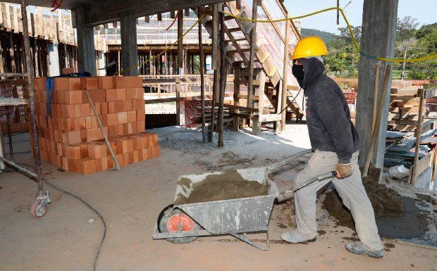 homem usando capacete e máscara empurra carrinho de mão em local de obra - vagas de emprego na grande florianópolis - consturção civil custotos preços