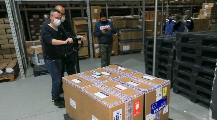 Doses da vacina Pfizer recebidas nesta terça-feira irão para 11 municípios quatro caixas de papelão com a doses de vacina da pfizer em galpão; homens de máscara em volta