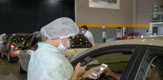 homem mostra dentro de carro celular com qr-code à funcionária de vacinação dentro de ginásio - vacinação de pessoas com comorbidades