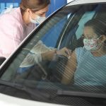 idosa recebe vacina no braço dentro de carro aplicada por mulher profissional de saúde