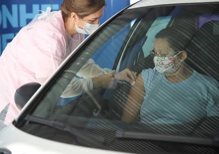idosa recebe vacina no braço dentro de carro aplicada por mulher profissional de saúde