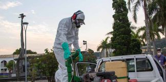 homem com trajes de proteção em cima de caçamba de pickup com equipamento de combate à dengue na praça do centro histórico