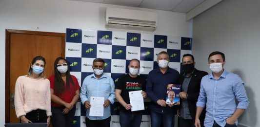 Sete pessoas lado a lado, usando máscaras, em ato simbólico de entrega de valor para construção da UBS Saveiro