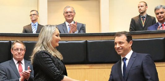 Em foto de arquivo, Daniela de roupa preta e cabelos loiros aperta a mão de Carlos Moisés, de terno escuro. Em volta é possível ver cinco homens de terno. O governador e a vice foram convocados para depor na CPI da pandemia, do senado federal.