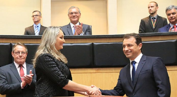 Em foto de arquivo, Daniela de roupa preta e cabelos loiros aperta a mão de Carlos Moisés, de terno escuro. Em volta é possível ver cinco homens de terno. O governador e a vice foram convocados para depor na CPI da pandemia, do senado federal.