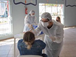 Um profissional de saúde com vestimentas de proteção se inclina com um cotonete em um paciente, para realizar o teste da covid. A partir de segunda, o CATI terá novo horário de atendimento para pacientes com sintomas respiratórios