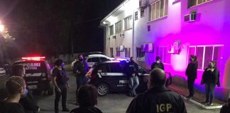 Policiais civis estão em circulo e uniformizados, no cenário ainda aparecem carros da polícia, eles cumpriram mandados e prenderam dois homens na operação de combate à pornografia infantojuvenil em Florianópolis