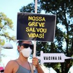 mulher usando máscara empunha placa escrita "nossa greve salvou vidas"