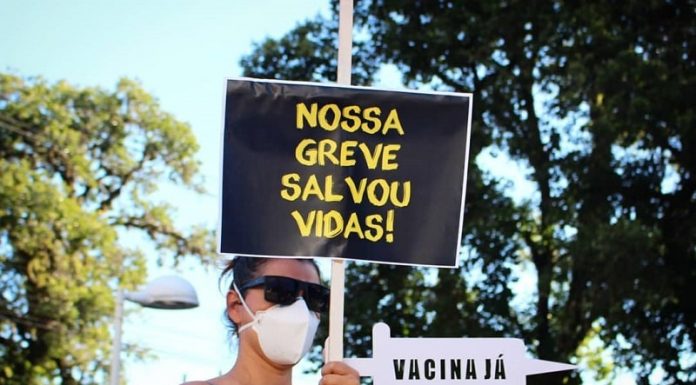 mulher usando máscara empunha placa escrita "nossa greve salvou vidas"