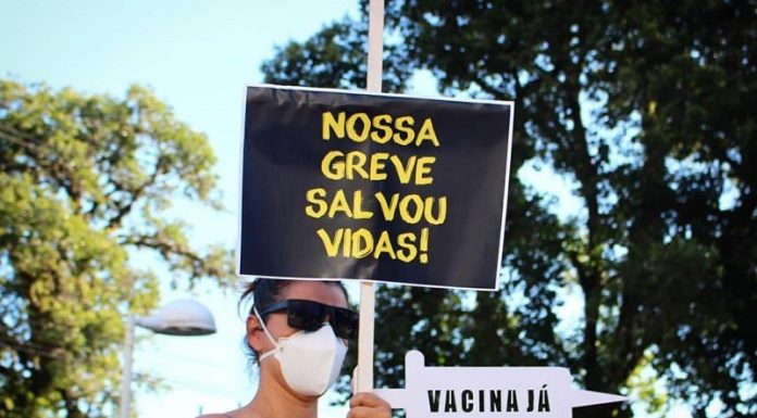 mulher usando máscara empunha placa escrita "nossa greve salvou vidas"