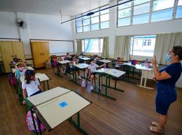 professora usando máscara dá aula para crianças em carteiras usando máscaras - doses para vacinação de professores