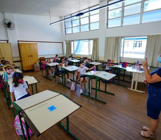 Municípios de SC têm 277 mil doses para iniciar vacinação em novos grupos professora usando máscara dá aula para crianças em carteiras usando máscaras - doses para vacinação de professores