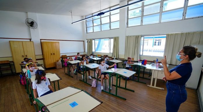 professora usando máscara dá aula para crianças em carteiras usando máscaras - doses para vacinação de professores