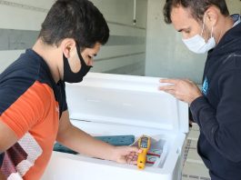 Novo lote de vacinas, com 209 mil doses, é distribuído em SC - homens conferem temperatura dentro de caixa de isopor