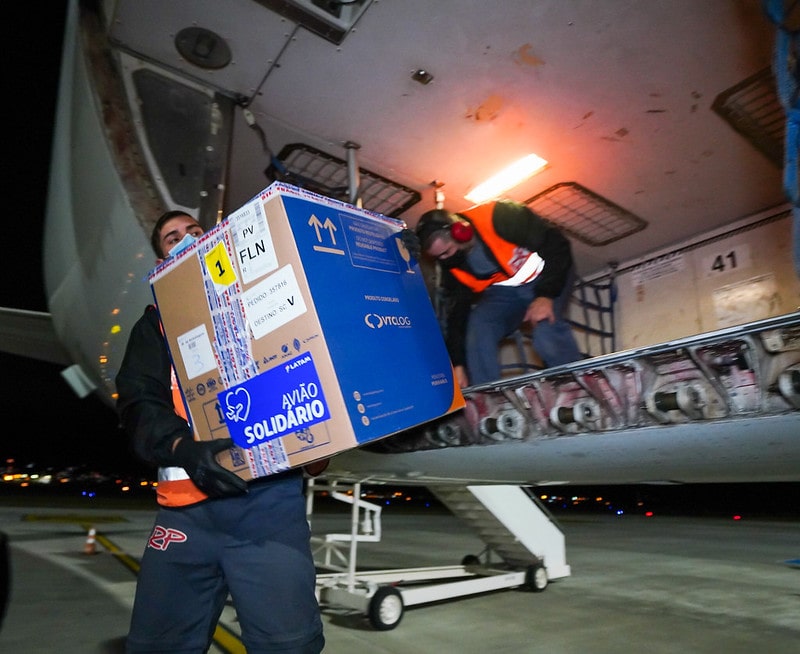 homem carrega caixa para fora de avião com doses de vacina