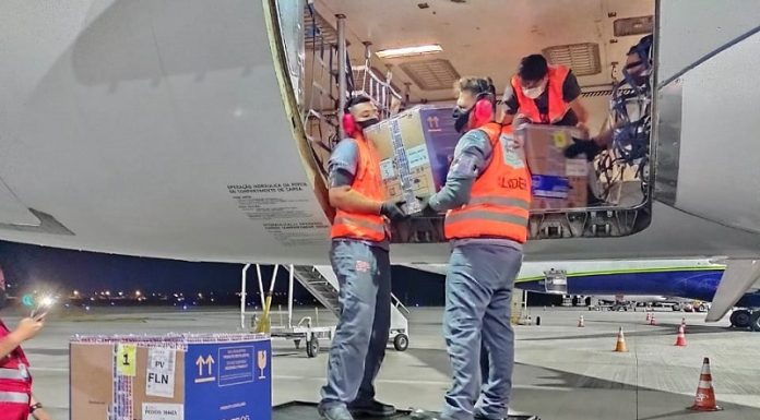 três homens retirando caixas de papelão do avião com as doses de vacina pfizer