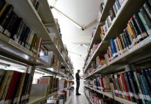 Homem em corredor de biblioteca com prateleiras cheias