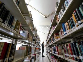 Homem em corredor de biblioteca com prateleiras cheias