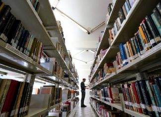 Homem em corredor de biblioteca com prateleiras cheias