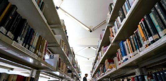 Homem em corredor de biblioteca com prateleiras cheias