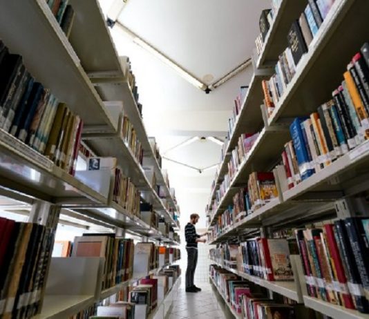 Homem em corredor de biblioteca com prateleiras cheias