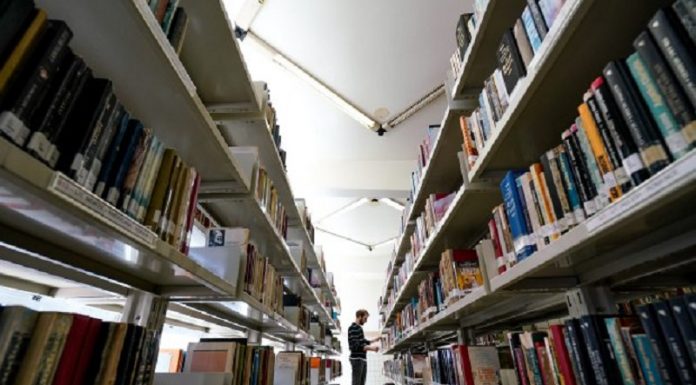 Homem em corredor de biblioteca com prateleiras cheias