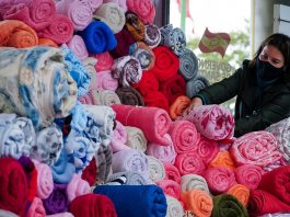 Com frio intenso, campanha cobertor solidário reforça pedido por doações Cobertores coloridos enrolados e empilhados, ao fundo uma mulher de preto os arruma. Eles fazem parte da campanha de doação cobertor solidário.