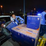 homens retirando de carro caixa de papelão com doses de vacina para distribuição