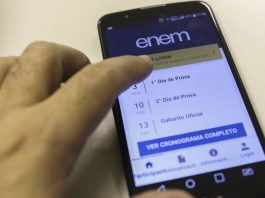 Uma mão mexe na tela de um celular em que é possível ler informações sobre o enem 2021