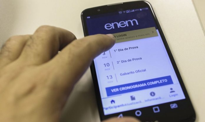 Uma mão mexe na tela de um celular em que é possível ler informações sobre o enem 2021