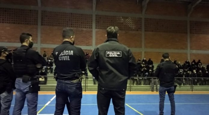 na deflagração da operação cova funda e cia policiais dentro de um ginásio: cinco em pé no meio da quadra e maioria sentada na arquibancada